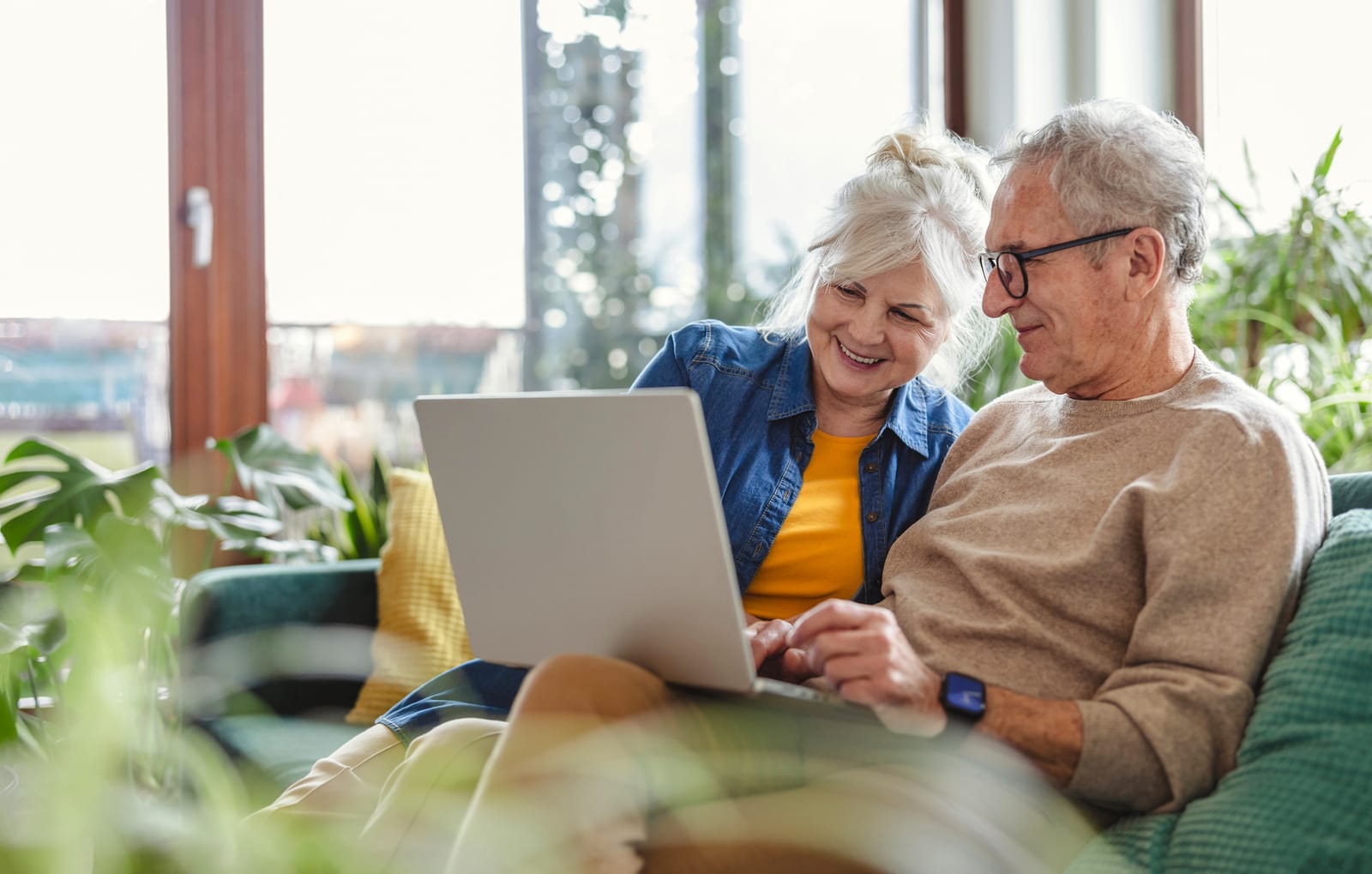 A smiling retired couple on their sofa looking at a laptop together